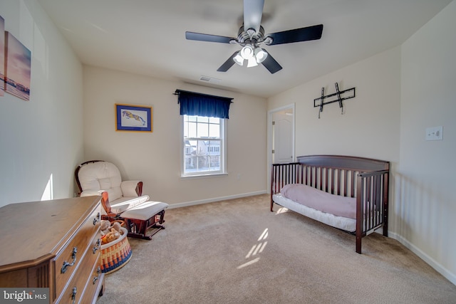 bedroom featuring ceiling fan, a crib, and light carpet