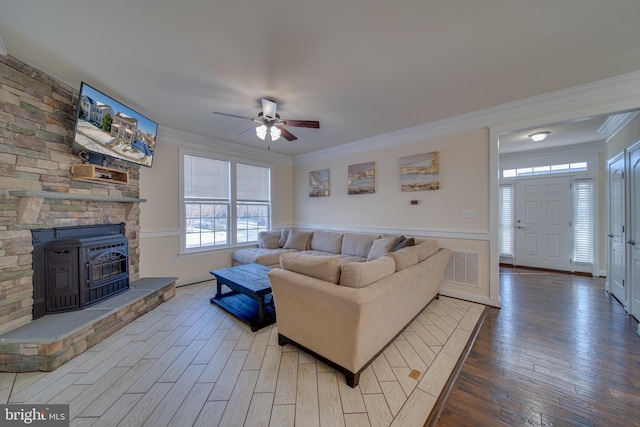 living room featuring hardwood / wood-style flooring, ceiling fan, a wood stove, and crown molding