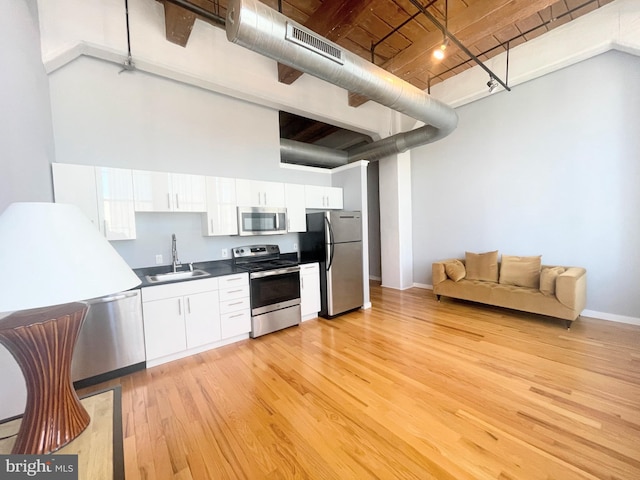 kitchen with appliances with stainless steel finishes, a towering ceiling, sink, light hardwood / wood-style floors, and white cabinetry