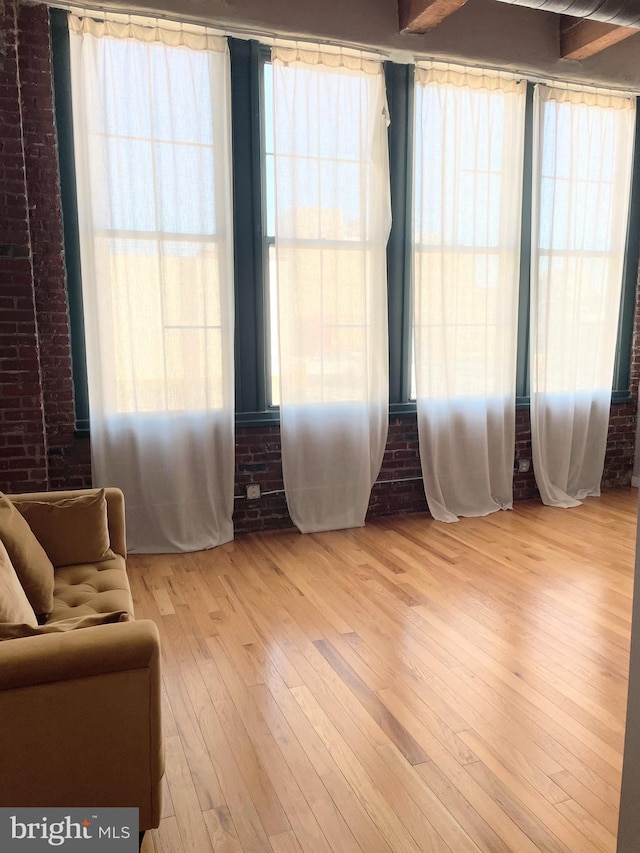 living area with a wealth of natural light, light hardwood / wood-style floors, and brick wall