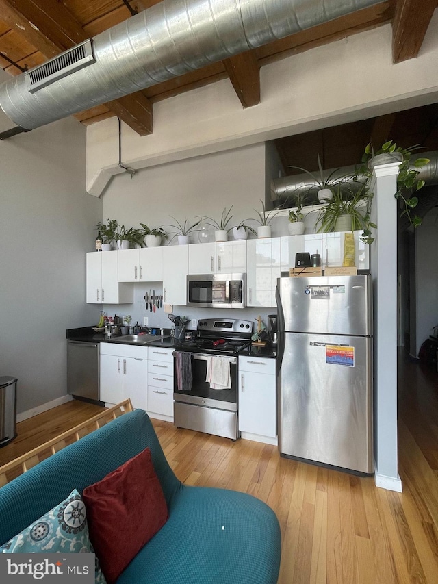 kitchen featuring white cabinetry, sink, beamed ceiling, light hardwood / wood-style floors, and appliances with stainless steel finishes