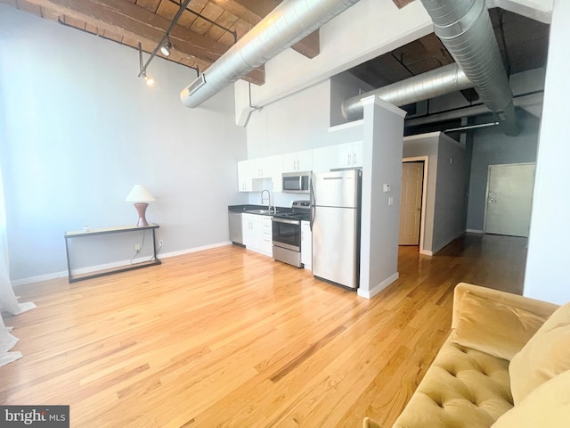 kitchen with light wood-type flooring, stainless steel appliances, sink, white cabinets, and a high ceiling