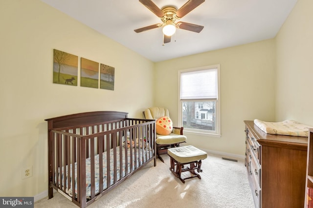 bedroom featuring ceiling fan, light carpet, and a crib