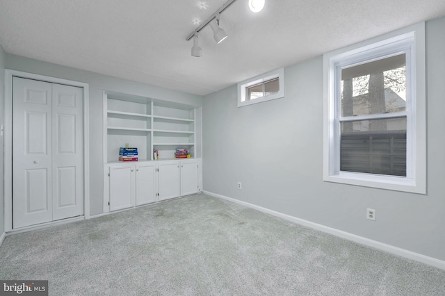 unfurnished bedroom with a textured ceiling, rail lighting, and light carpet