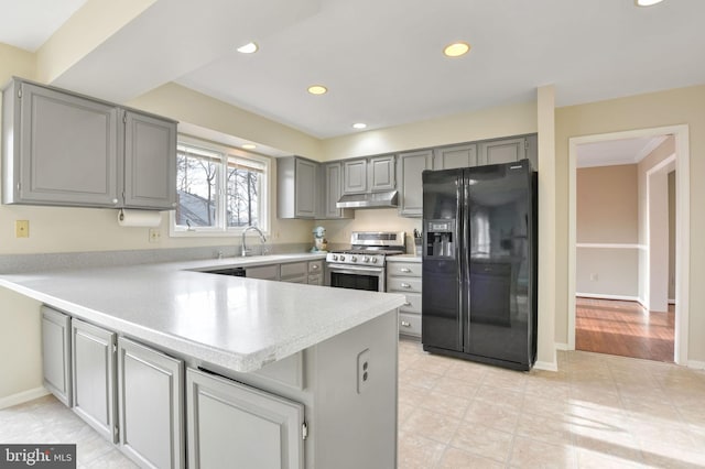 kitchen featuring gray cabinetry, black fridge, sink, kitchen peninsula, and stainless steel range with gas stovetop