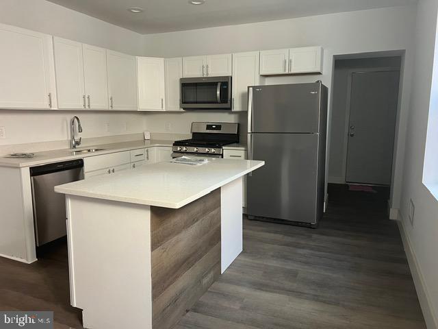 kitchen featuring white cabinets, sink, dark hardwood / wood-style floors, appliances with stainless steel finishes, and a kitchen island