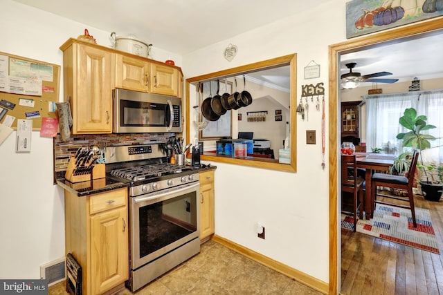 kitchen featuring dark stone counters, ceiling fan, ornamental molding, light brown cabinetry, and appliances with stainless steel finishes