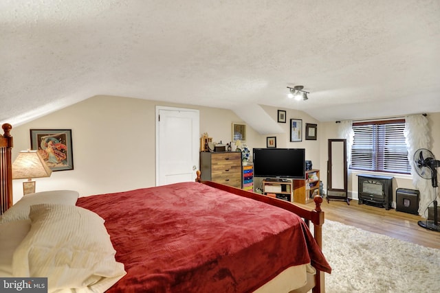 bedroom with lofted ceiling, light wood-type flooring, a textured ceiling, and a wood stove