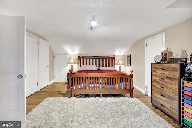 bedroom featuring wood-type flooring, a textured ceiling, and vaulted ceiling