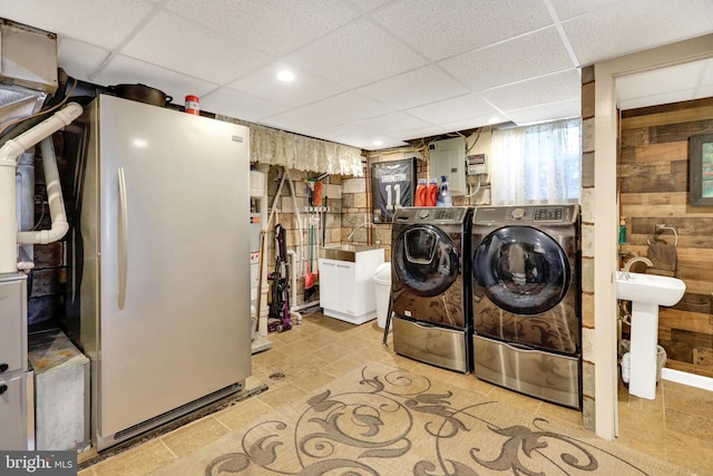 clothes washing area featuring washing machine and clothes dryer, wood walls, and gas water heater