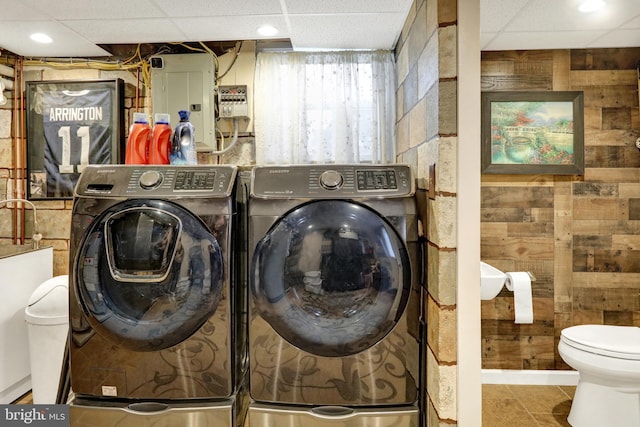 washroom featuring washing machine and dryer, wood walls, and electric panel