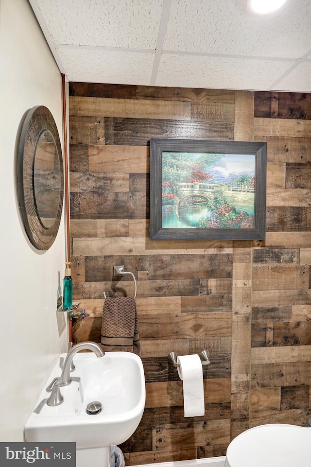 bathroom featuring a drop ceiling, wooden walls, and sink