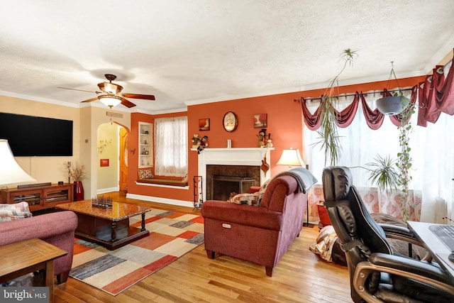 living room with a textured ceiling, light hardwood / wood-style flooring, ceiling fan, and ornamental molding