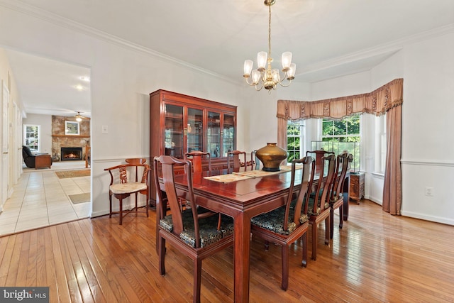 dining space with a fireplace, light hardwood / wood-style floors, ceiling fan with notable chandelier, and ornamental molding