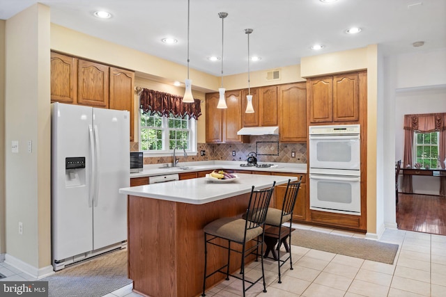 kitchen with pendant lighting, a center island, white appliances, sink, and light tile patterned flooring