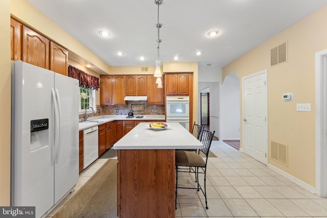 kitchen featuring a center island, decorative light fixtures, white appliances, a kitchen bar, and decorative backsplash