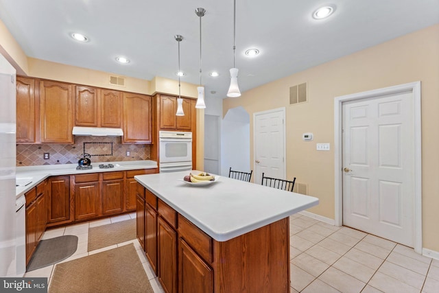 kitchen featuring a center island, white appliances, backsplash, hanging light fixtures, and light tile patterned floors