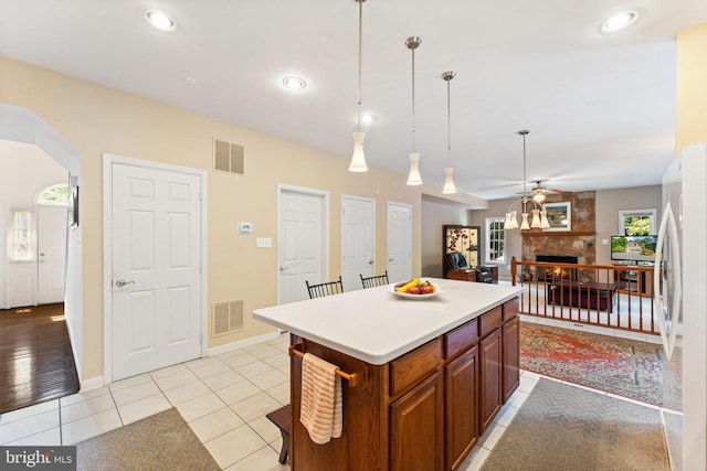 kitchen featuring pendant lighting, white refrigerator, a kitchen island, a fireplace, and light tile patterned flooring