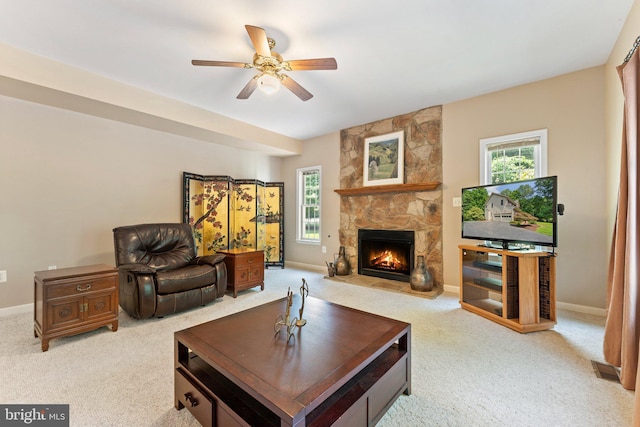 carpeted living room featuring a stone fireplace, a wealth of natural light, and ceiling fan