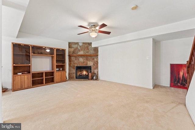 unfurnished living room featuring light colored carpet, a stone fireplace, and ceiling fan