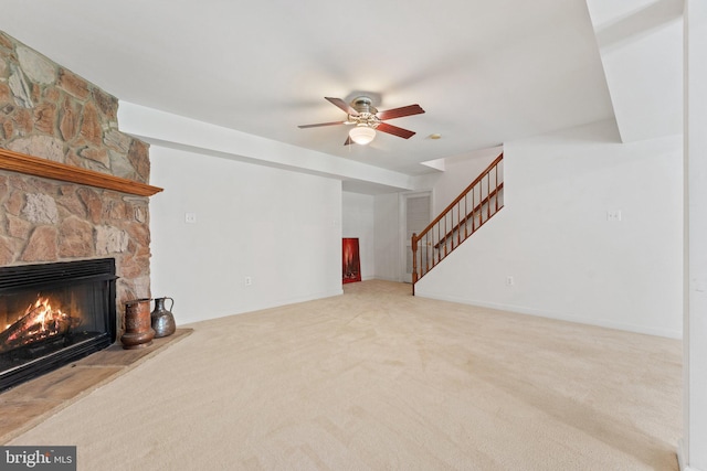 unfurnished living room with carpet, a stone fireplace, and ceiling fan