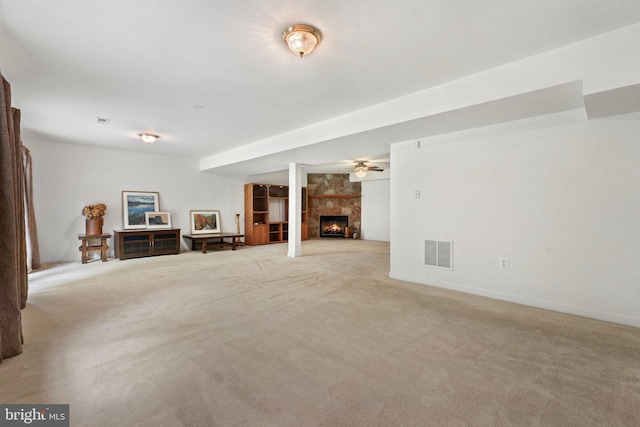 unfurnished living room with ceiling fan, a stone fireplace, and light carpet