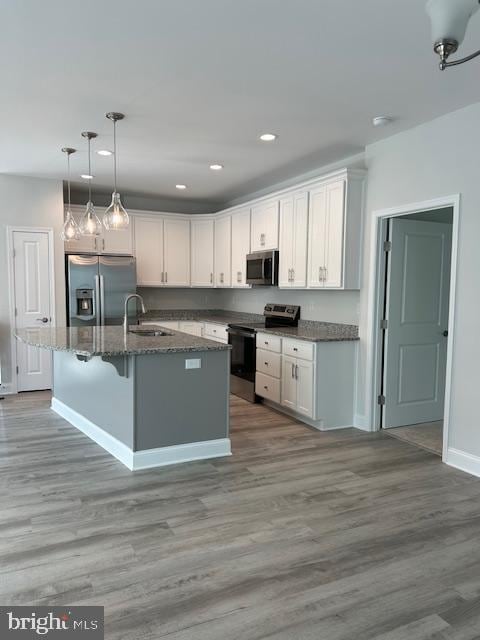 kitchen featuring appliances with stainless steel finishes, sink, white cabinets, hanging light fixtures, and an island with sink