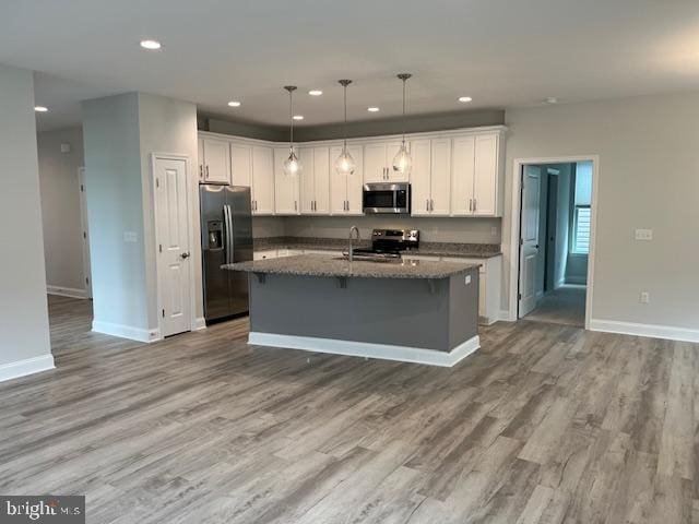 kitchen with white cabinetry, a kitchen island with sink, hanging light fixtures, and stainless steel appliances