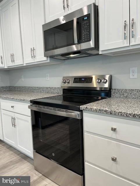 kitchen featuring appliances with stainless steel finishes, light wood-type flooring, white cabinetry, and light stone counters