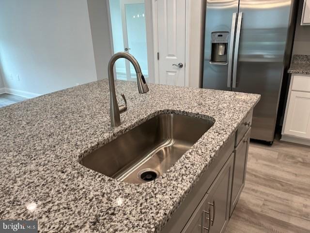 kitchen with white cabinets, stainless steel fridge, light stone counters, and sink