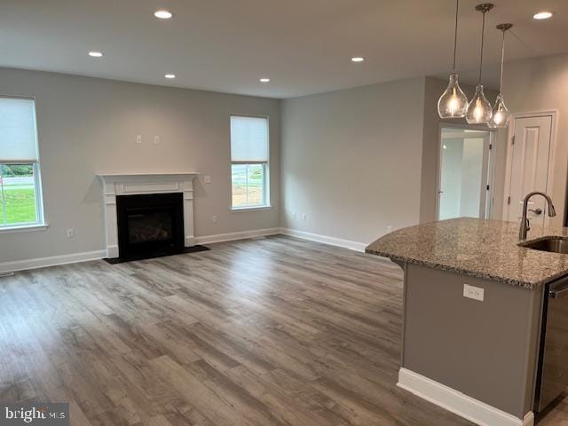 kitchen featuring light stone counters, stainless steel dishwasher, sink, decorative light fixtures, and dark hardwood / wood-style floors