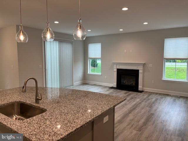 kitchen with hanging light fixtures, light stone counters, a wealth of natural light, and sink