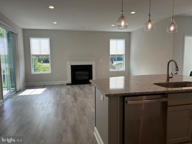 kitchen featuring dishwasher, sink, light stone counters, light hardwood / wood-style floors, and decorative light fixtures