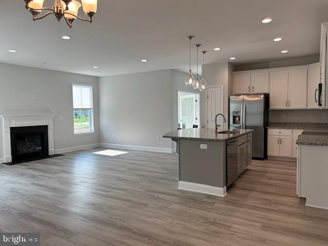 kitchen featuring a kitchen island with sink, an inviting chandelier, white cabinets, decorative light fixtures, and stainless steel appliances