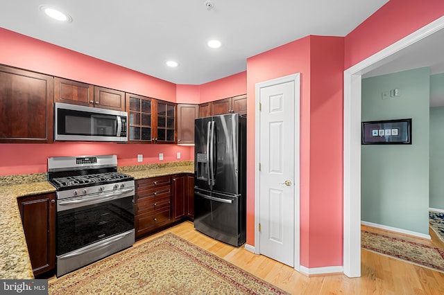 kitchen with light stone countertops, dark brown cabinets, stainless steel appliances, and light hardwood / wood-style floors