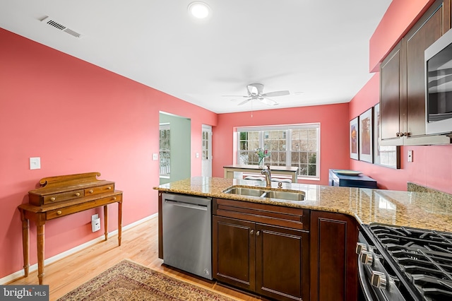 kitchen with light wood-type flooring, appliances with stainless steel finishes, light stone counters, and sink