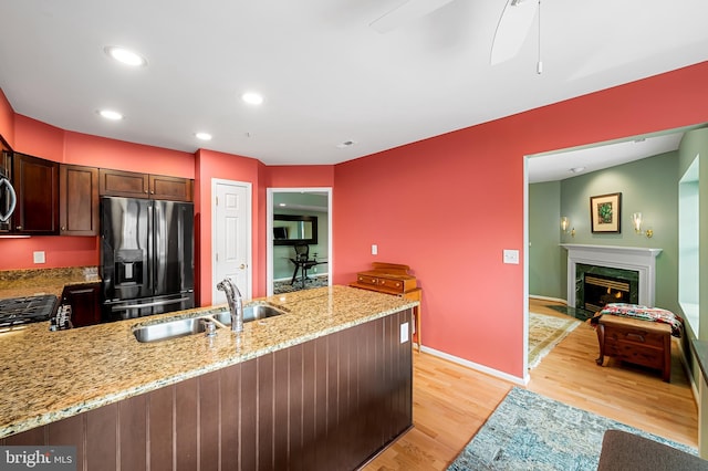 kitchen with kitchen peninsula, stainless steel appliances, light hardwood / wood-style flooring, light stone counters, and sink