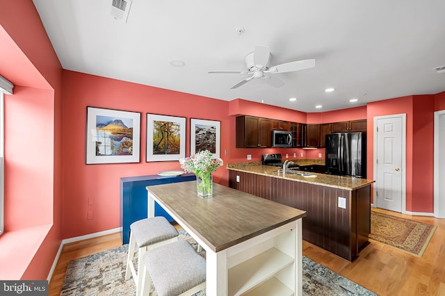 kitchen with black refrigerator with ice dispenser, a kitchen bar, light hardwood / wood-style floors, sink, and ceiling fan