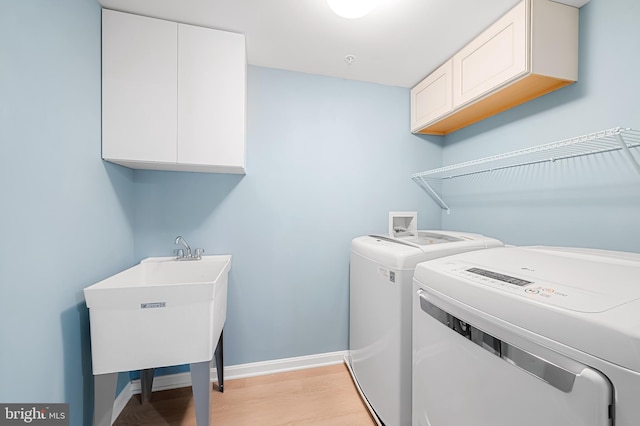 washroom featuring washer and clothes dryer, sink, light hardwood / wood-style floors, and cabinets