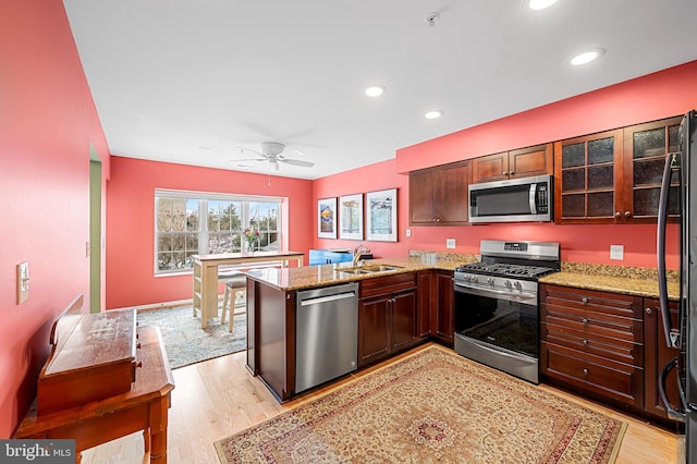 kitchen featuring appliances with stainless steel finishes, light hardwood / wood-style floors, sink, kitchen peninsula, and ceiling fan