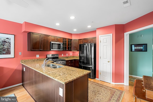 kitchen with light hardwood / wood-style floors, light stone countertops, kitchen peninsula, and stainless steel appliances