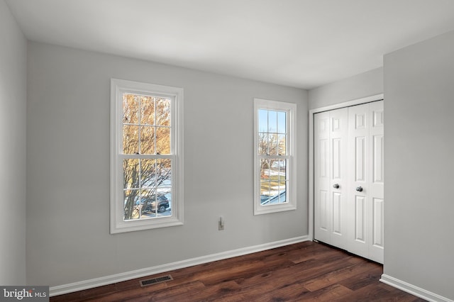 unfurnished bedroom featuring a closet, multiple windows, and dark hardwood / wood-style floors