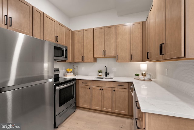 kitchen with sink, appliances with stainless steel finishes, light stone counters, decorative backsplash, and light wood-type flooring