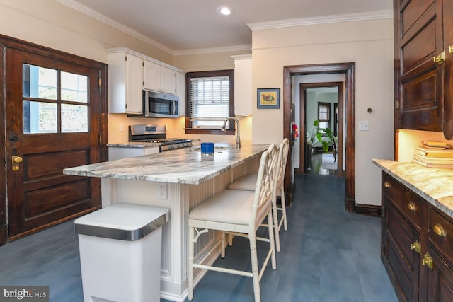 kitchen with white cabinets, crown molding, a breakfast bar area, light stone countertops, and stainless steel appliances