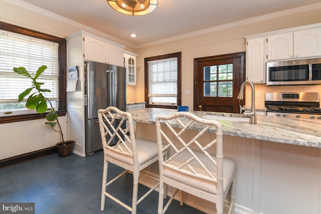 kitchen featuring white cabinetry, light stone countertops, a breakfast bar, appliances with stainless steel finishes, and ornamental molding