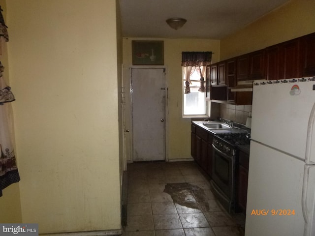 kitchen with sink, backsplash, black gas stove, white fridge, and dark brown cabinets