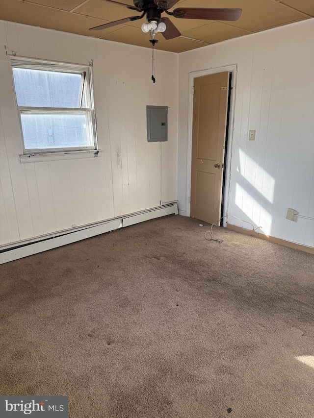 spare room with ceiling fan, baseboard heating, electric panel, wood walls, and carpet floors