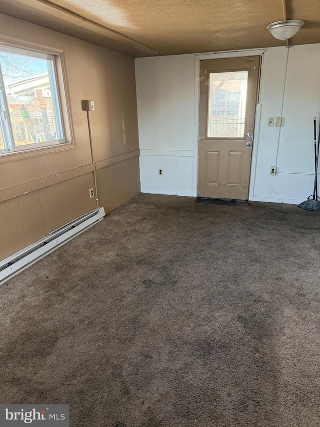 foyer featuring dark carpet, a textured ceiling, and a baseboard heating unit