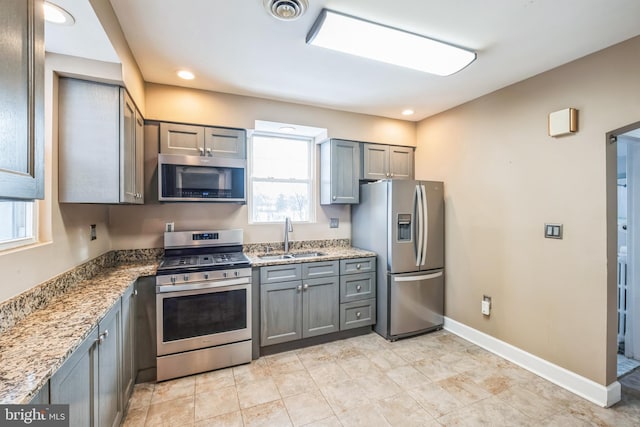 kitchen featuring light stone counters, appliances with stainless steel finishes, gray cabinetry, and sink