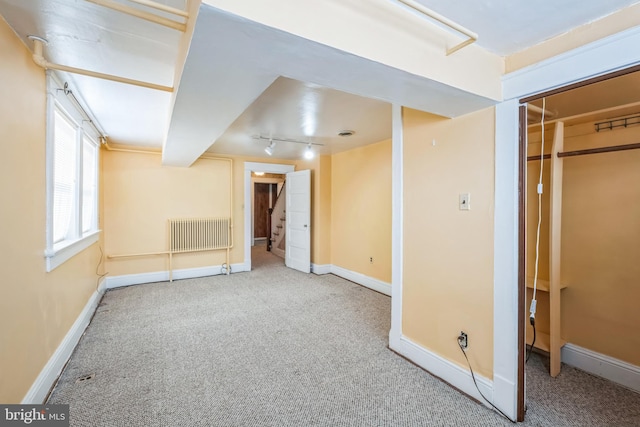 basement featuring track lighting, carpet flooring, and radiator heating unit